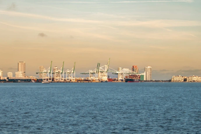 A harbor scene features cargo cranes and city buildings.